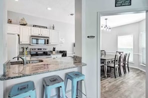 A modern kitchen with white cabinets, a granite countertop, and a dining area with a table and chairs.