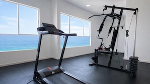 Un gimnasio con cinta de correr, banco para pesas y mancuernas, con amplias ventanas que ofrecen vistas al océano.