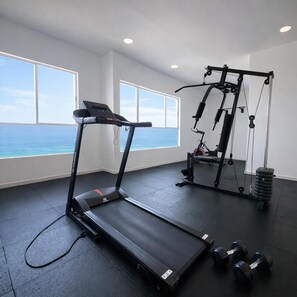 Un gimnasio con cinta de correr, banco para pesas y mancuernas, con amplias ventanas que ofrecen vistas al océano.