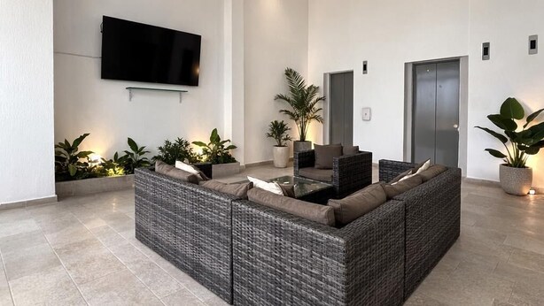 Una sala de estar moderna con un sofá modular grande, un televisor de pantalla plana montado en la pared y plantas en macetas.