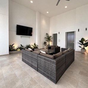 Una sala de estar moderna con un sofá modular grande, un televisor de pantalla plana montado en la pared y plantas en macetas.