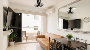 Una sala de estar moderna con sofá, mesa de comedor, sillas, televisor y balcón con vistas.
