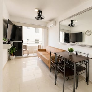 Una sala de estar moderna con sofá, mesa de comedor, sillas, televisor y balcón con vistas.