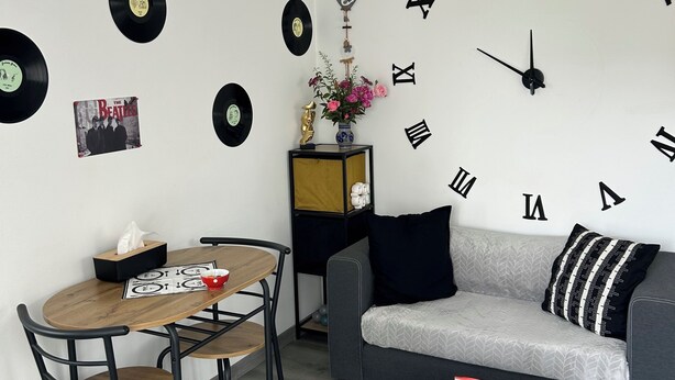 A modern living room with a round dining table, a sofa, and a wall clock. - Charming full T1 (Zillisheim)