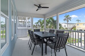 A covered porch with a table and chairs, a ceiling fan, and a view of palm trees and houses. - Dolphin Run | Heated Pool, 3-Min Walk to Beach! (Fort Myers Beach)
