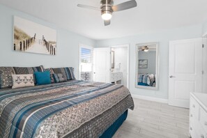 A bedroom with a bed, a ceiling fan, a large mirror, and a door. - Dolphin Run | Heated Pool, 3-Min Walk to Beach! (Fort Myers Beach)