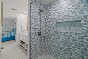 A bathroom with a glass shower enclosure, a white sink, and a blue bed in the adjacent room. - Dolphin Run | Heated Pool, 3-Min Walk to Beach! (Fort Myers Beach)