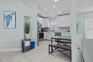 A modern kitchen with white cabinets, a dining table, and a potted plant. - Dolphin Run | Heated Pool, 3-Min Walk to Beach! (Fort Myers Beach)