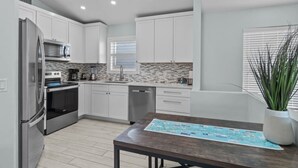 A modern kitchen with white cabinets, a stainless steel refrigerator, and a wooden dining table. - Dolphin Run | Heated Pool, 3-Min Walk to Beach! (Fort Myers Beach)