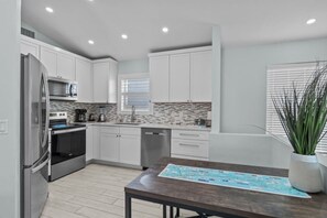 A modern kitchen with white cabinets, a stainless steel refrigerator, and a wooden dining table. - Dolphin Run | Heated Pool, 3-Min Walk to Beach! (Fort Myers Beach)