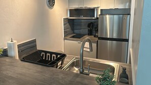 Et moderne køkken med et rustfrit stål køleskab, en indbygget ovn, en mikroovn og en vask med armatur. Der er et ur på væggen og en lille plantepotte på bordet.