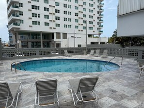 A rooftop swimming pool with lounge chairs and a modern building in the background. - Ocean Breeze Studio (Carolina)