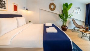 Camera d'albergo con un letto, una pianta in vaso, una sedia e un tavolino con un bicchiere da vino e una candela.