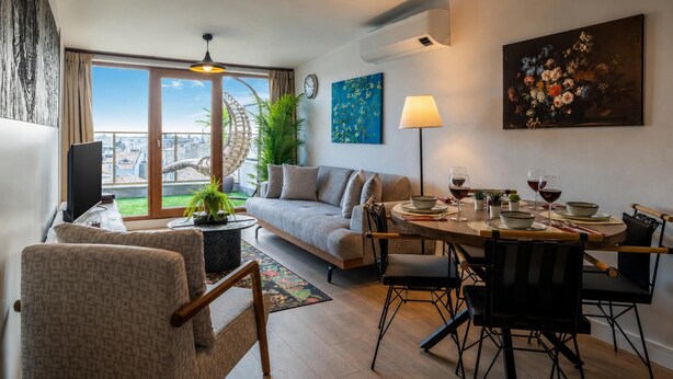 Un soggiorno moderno con divano, tavolo da pranzo, sedie, televisore e una grande finestra vista città.