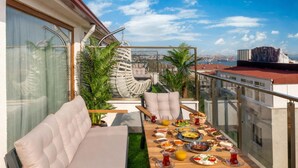 Una terrazza sul tetto con un tavolo apparecchiato per un pasto, posti a sedere imbottiti e piante in vaso.