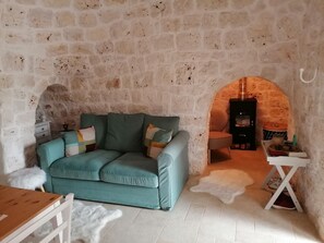 Ein gemütlicher Raum mit Steinwand, einem petrolfarbenen Sofa, einem kleinen Tisch und einem Kamin.