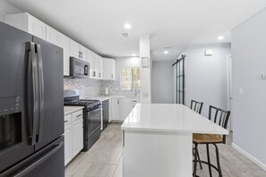 Eine moderne Küche mit weißen Schränken, einem Edelstahlkühlschrank, einer Mikrowelle, einem Backofen und einer großen Kochinsel mit Barhocker.