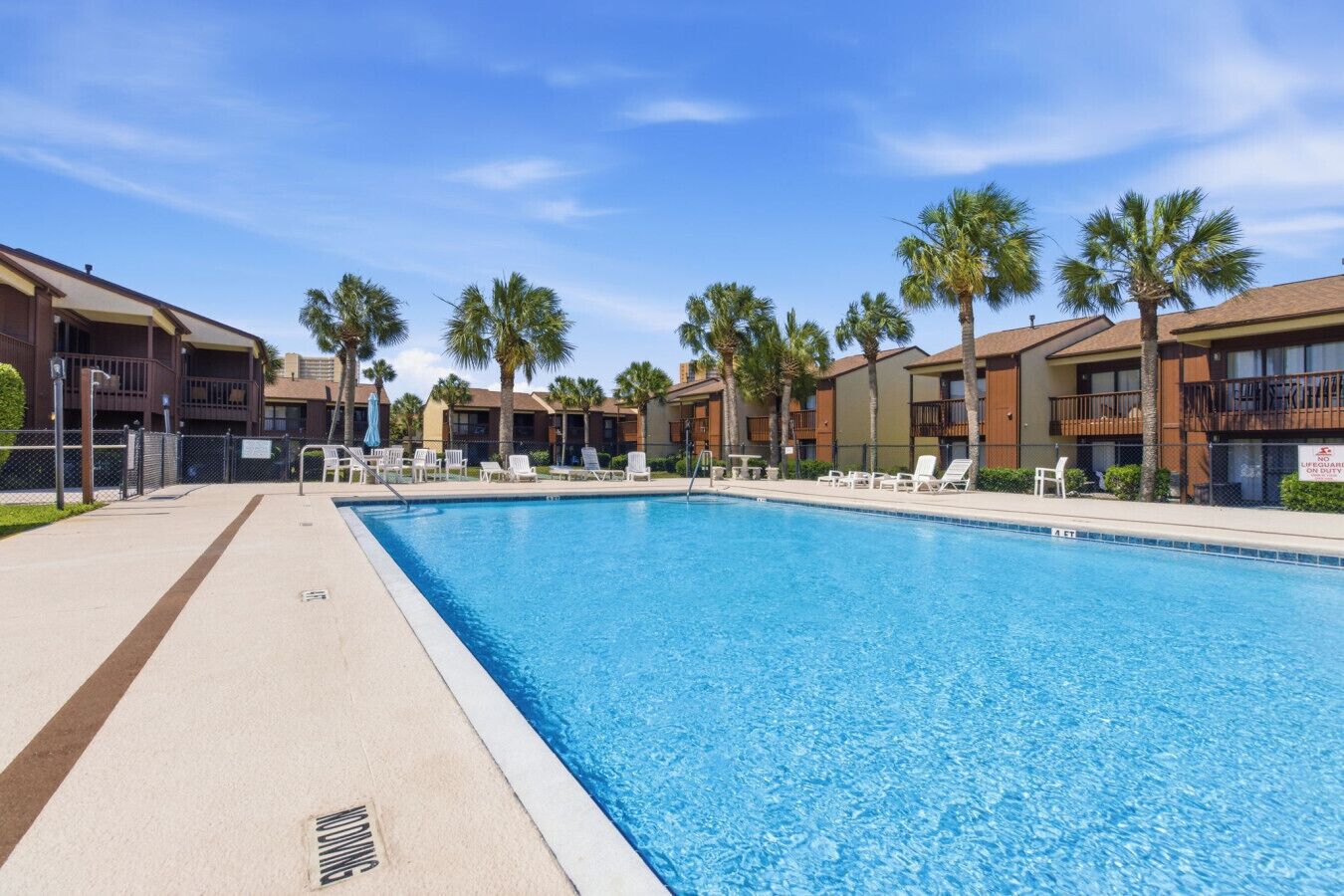 A swimming pool with lounge chairs, palm trees, and a clear blue sky.