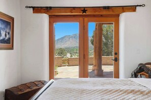 Ein Schlafzimmer mit einem großen Bett, einer Holztür zu einer Terrasse im Freien mit Blick auf die Berge.