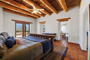 Ein Schlafzimmer mit einem Bett, Holzbalken, einem Deckenventilator und Blick durch eine Tür.
