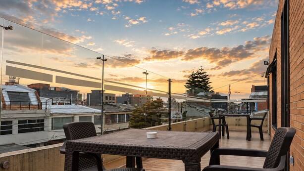 A rooftop terrace with a table and chairs, overlooking a cityscape at sunset. - Suit Double 304 with Sale + Kitchen and Laundry (Bogotá)