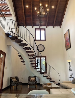 Un vaste espace de vie agrémenté d’un escalier en courbe, d’un lustre, d’une horloge et d’un lampadaire.