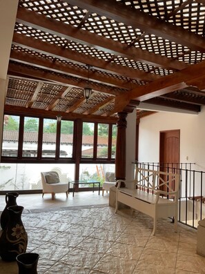 Ein geräumiges Zimmer mit hohen Decken, Holzbalken, großen Fenstern und einem Balkon.