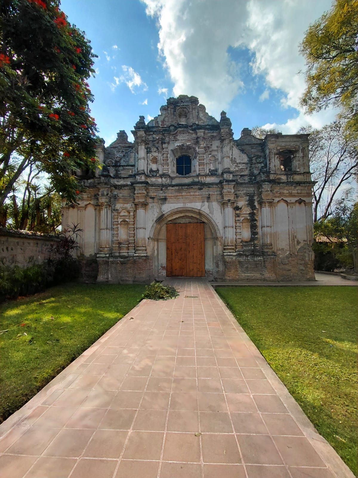 An ancient stone building with a large wooden door, surrounded by a well-maintained lawn and trees.