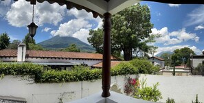 Ein Balkon mit Blick auf einen Berg, ein weißes Gebäude mit Ziegeldach und ein Baum im Vordergrund.
