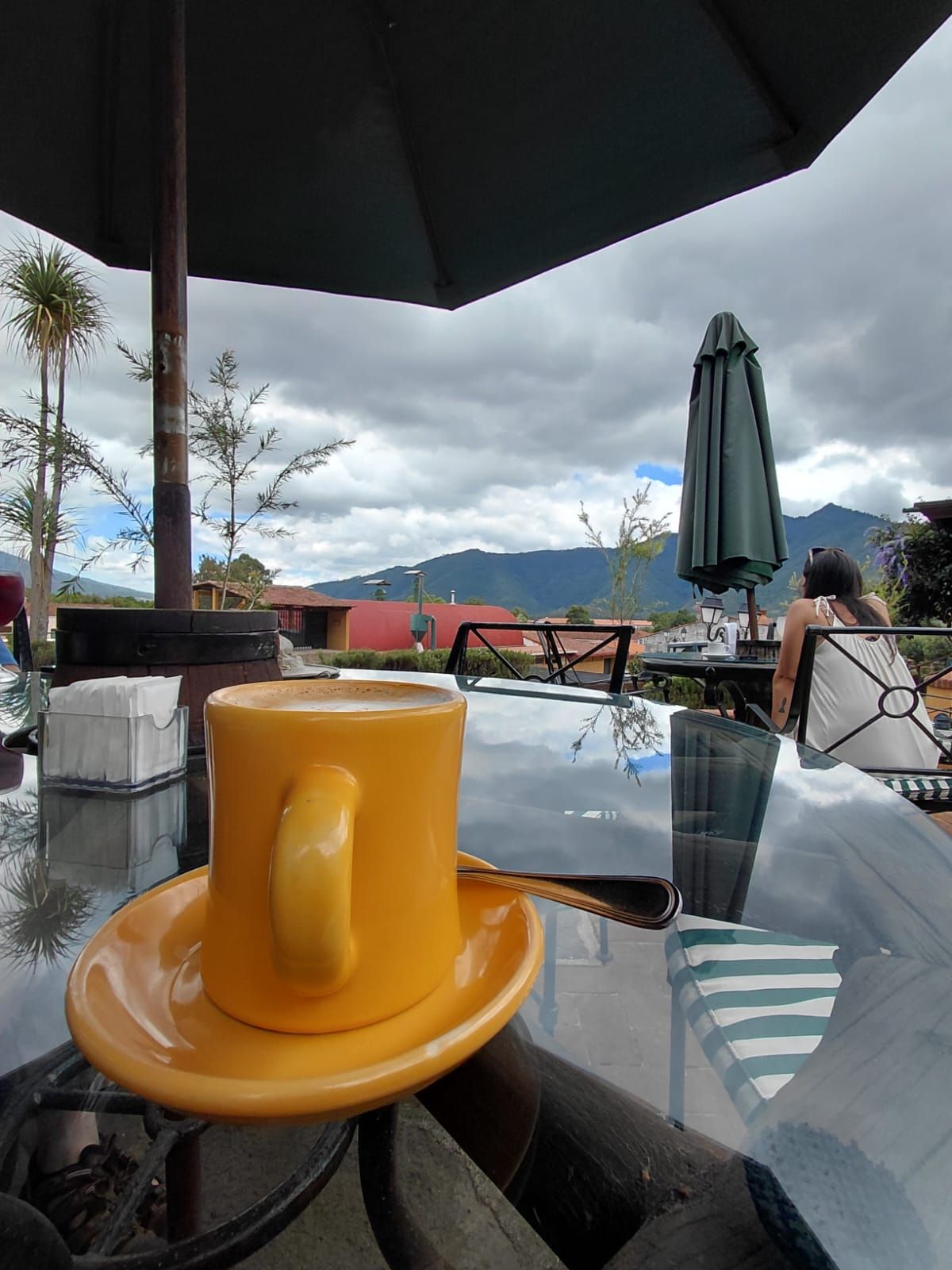 A table with a yellow mug and saucer, a glass table, and an umbrella.