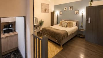Une chambre à coucher avec un lit, des tables de chevet, un bureau avec une chaise, une petite plante et une porte.