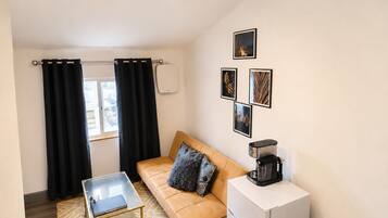 Un espacio habitable compacto con sofá, cafetera, pequeña mesa y refrigerador.