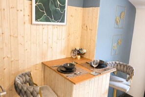 Ein kleiner Essbereich mit einem Holztisch, zwei Stühlen, einer Schüssel mit Snacks und einem Weinglas.