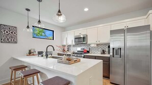 A modern kitchen with white cabinets, stainless steel appliances, pendant lighting, and a large island with stools. - SoCo 2BR South Austin Modern Gem & Very Walkable! (Austin)
