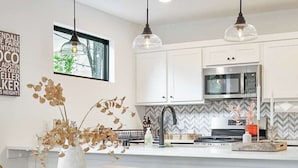 A modern kitchen with white cabinets, a microwave, and a dining area with a wooden table and chairs. - SoCo 2BR South Austin Modern Gem & Very Walkable! (Austin)