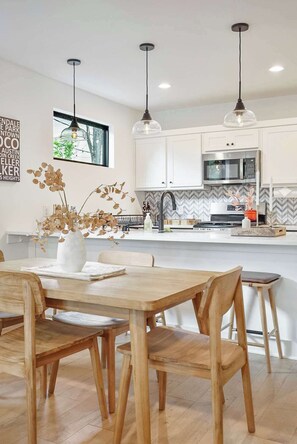 Eine moderne Küche mit weißen Schränken, einer Mikrowelle und einem Essbereich mit einem Holztisch und Stühlen.