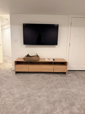 A room with a flat-screen TV mounted on the wall, a wooden console table with drawers, and a carpeted floor.