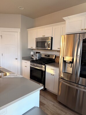 A modern kitchen with white cabinetry, stainless steel appliances, and a wooden floor.