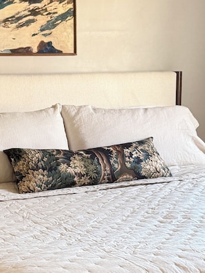 Un lit avec une couette blanche et deux oreillers, dont un uni et l’autre à motifs floraux.