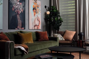 Una sala de estar con un sofá verde, una mesa de centro negra y una planta grande.