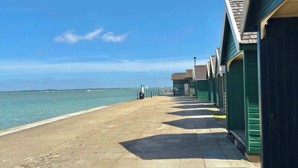 A seaside promenade with a row of green buildings, a clear sky, and calm waters. - Stylish Coastal Cottage in Gurnard, Dog Friendly Garden (Cowes)