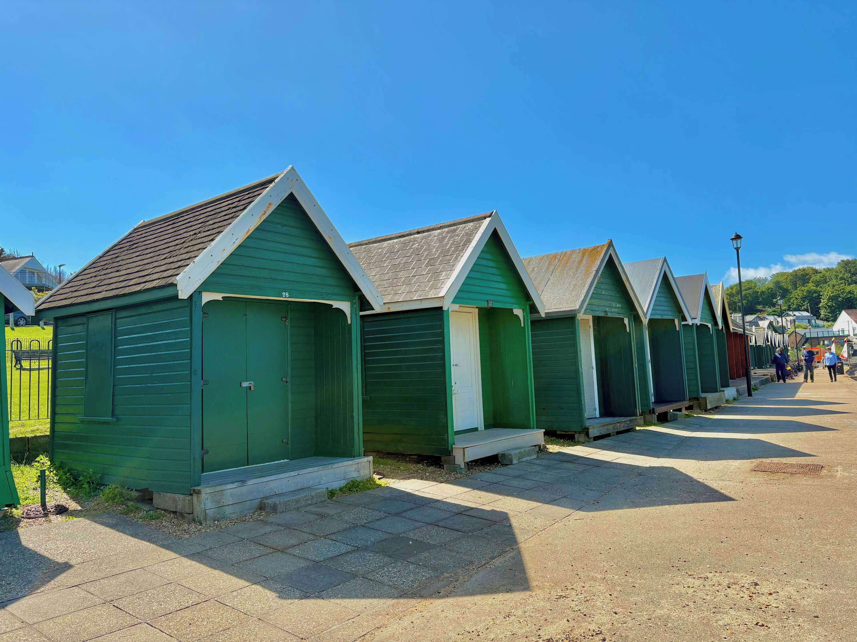 A row of green beach huts with a tiled walkway in between.