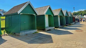 A row of green beach huts with a tiled walkway in between. - Stylish Coastal Cottage in Gurnard, Dog Friendly Garden (Cowes)