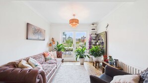 A living room with a sofa, a coffee table, and a dining area with a table and chairs. There are potted plants and a hanging light fixture. - Stylish Coastal Cottage in Gurnard, Dog Friendly Garden (Cowes)