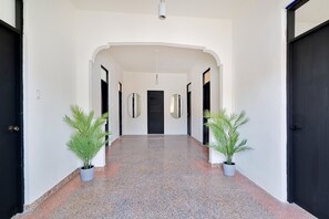 Un pasillo con piso pulido, dos plantas en macetas y una puerta negra al final.