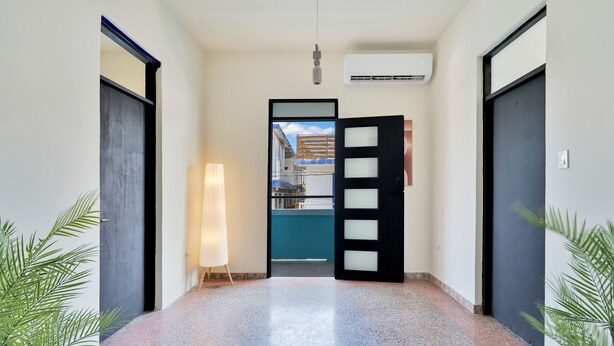 Un couloir avec un luminaire, un appareil de climatisation et une porte donnant sur une pièce.