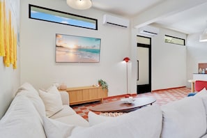 Een moderne woonkamer met een bank, een salontafel, een schilderij van een strand en een rode vloerlamp.