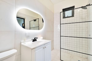 Un baño con lavamanos blanco, espejo y cabina de ducha.