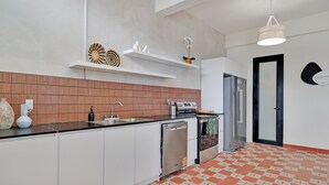 Une cuisine moderne avec des meubles blancs, un lave-vaisselle et un réfrigérateur. On y trouve des étagères ornées d’objets décoratifs et un sol à motifs.