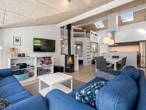 Ein modernes Wohnzimmer mit Kamin, Fernseher und Essbereich, im Hintergrund eine Küche.